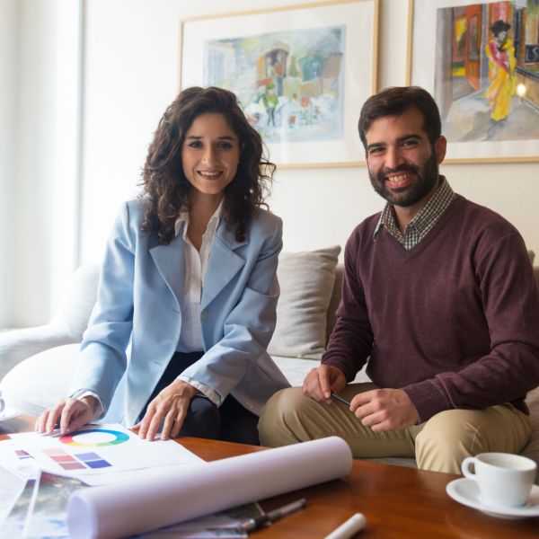 Happy interior designer and client discussing renovation, studying swatches, sketches and blueprints. Young man and woman sitting in living room at home and talking. Working on home design concept